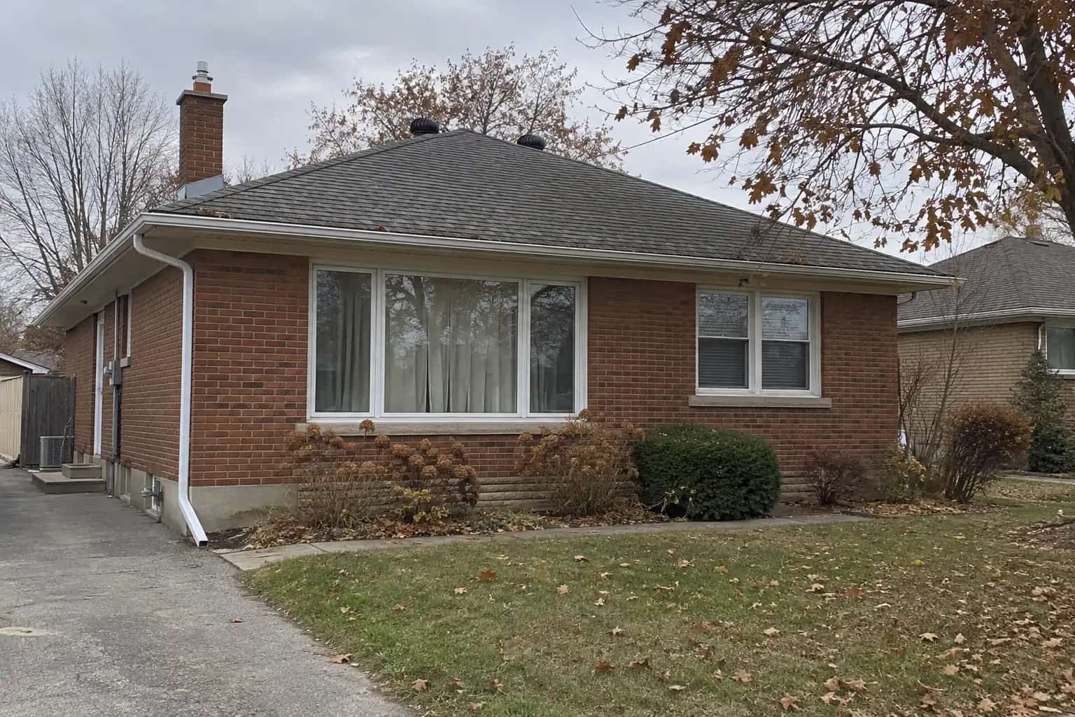 Brick bungalow with a weathered grey hip roof, roof vents and a few autumn leaves along the gutter.