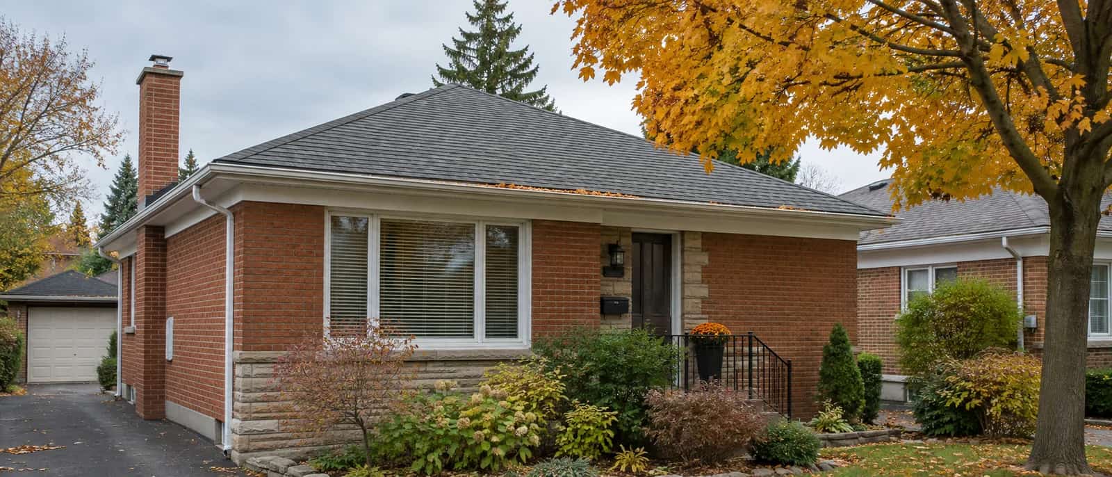 A brick bungalow with autumn leaves along its front eavestrough