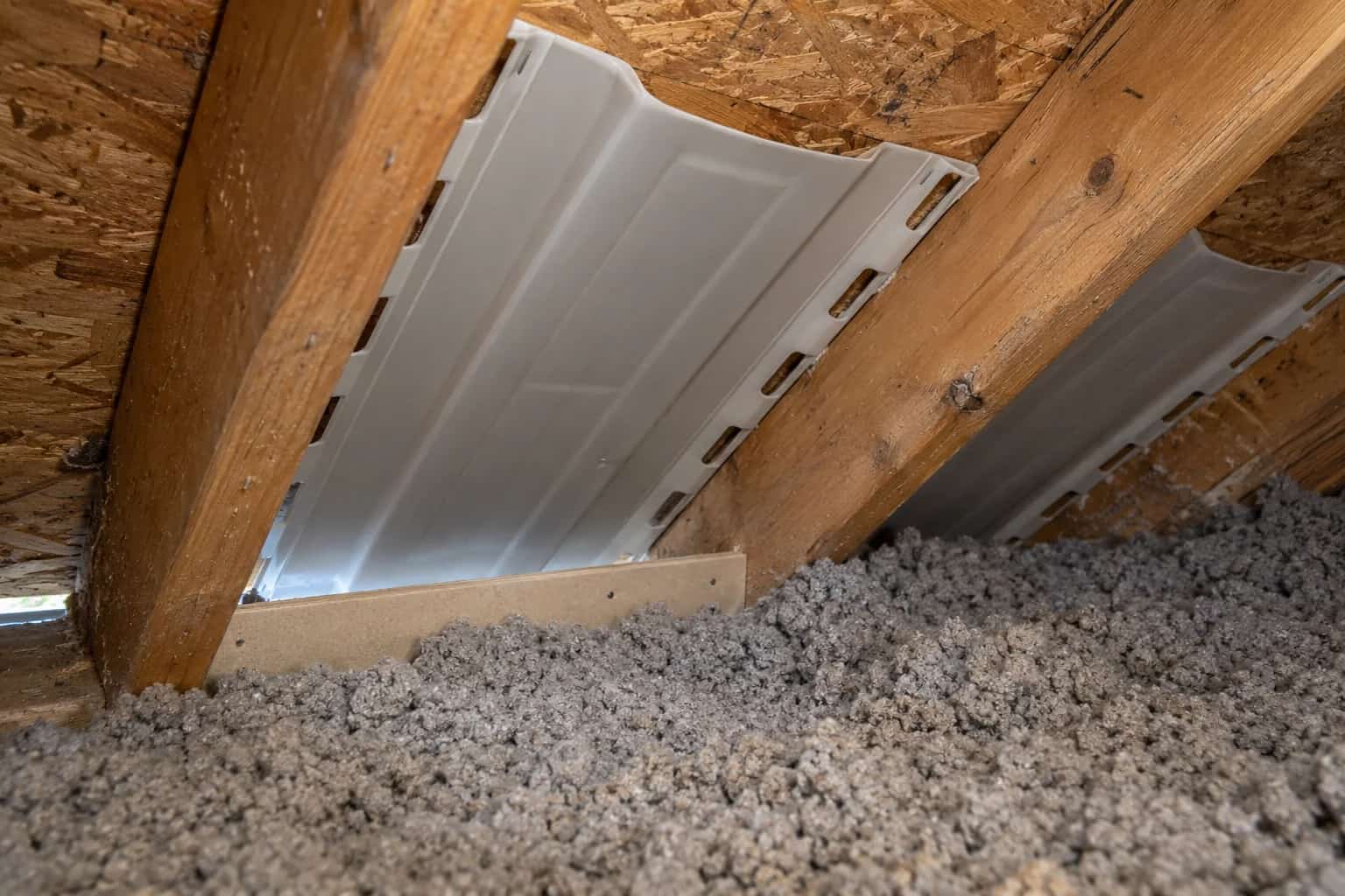 Pale attic baffles between timber rafters above grey loose-fill insulation.