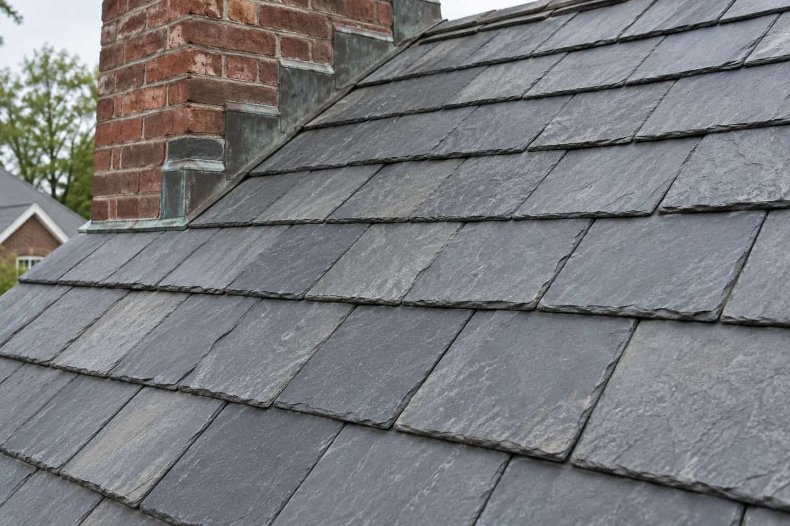Grey natural slate tiles in overlapping courses beside a brick chimney and stepped flashing.