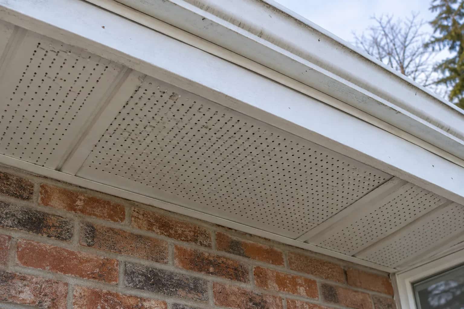 Perforated white soffit panels with weathered paint along several openings.